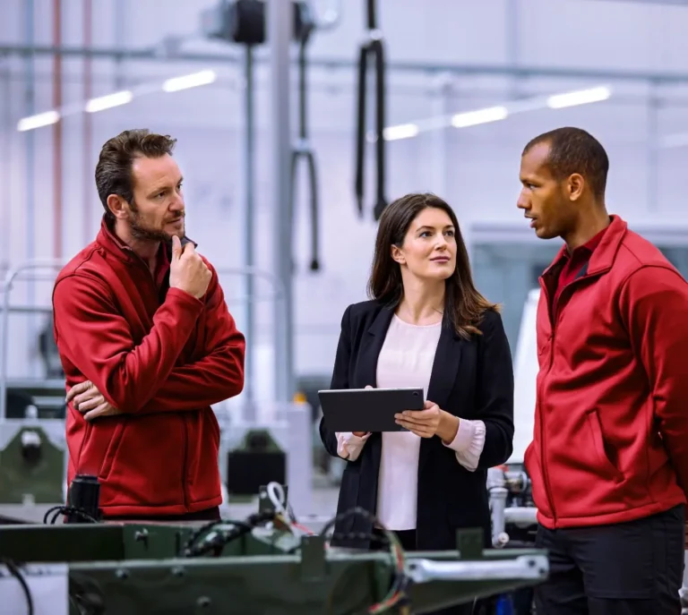 3 people in a factory. One of them has a tablet in their hands.
