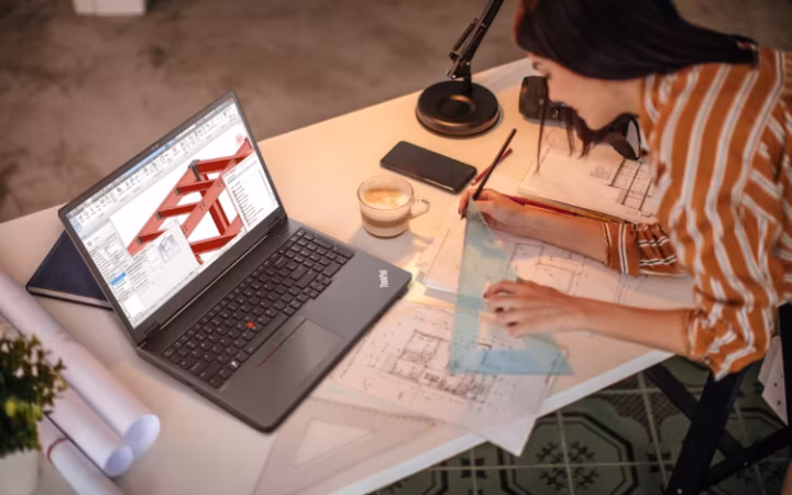 A person working on architectural plans with an open laptop