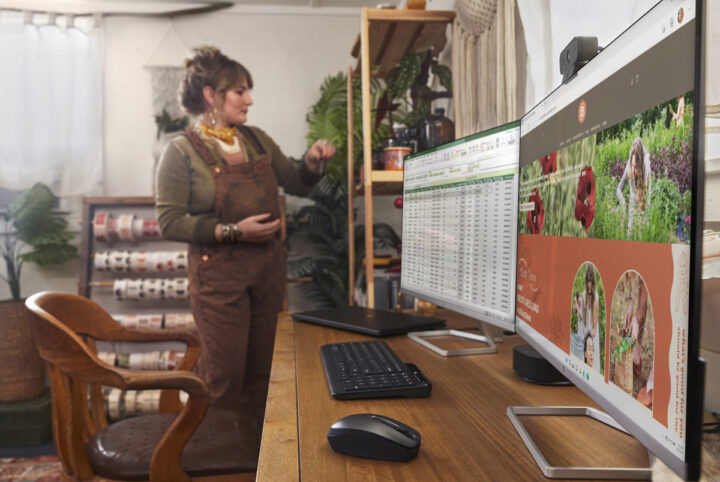 2 large monitors in the foreground and a person standing in the background